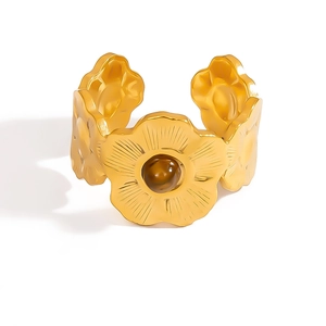 Dettaglio del bracciale aperto dorato con motivi floreali e gemma marrone centrale