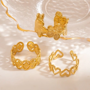 Three gold stainless steel adjustable open rings with flower and heart designs on a tray
