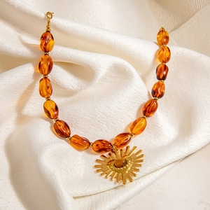 Vintage amber resin beaded necklace with a golden sunburst pendant on white fabric