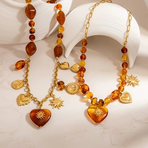 Detail of amber resin bead necklace with 18K gold plated heart pendant and solar charms