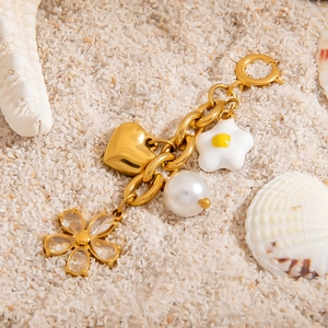 Nahaufnahme goldener Bikini-Anhänger mit Herz, Perle und Blumen auf dem Strandsand