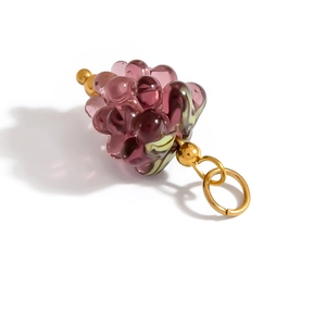 Macro detail of a purple glass grape charm with golden metal leaf and ring connector