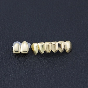 Close-up of gold-plated 2-tooth and 6-tooth hip hop grills on black leather surface