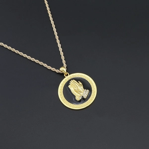 Close-up of golden prayer hands pendant with rhinestone cuff and Greek key pattern border