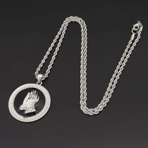 Macro detail of silver praying hands pendant with white rhinestones and greek fret border