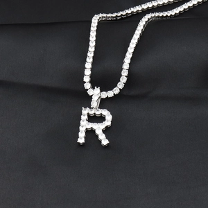 Détail du pendentif lettre R argenté serti sur une chaîne tennis sur fond de soie noire