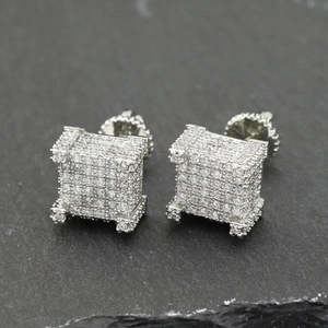 Detail of silver square iced-out earrings with white zircon on a dark slate background