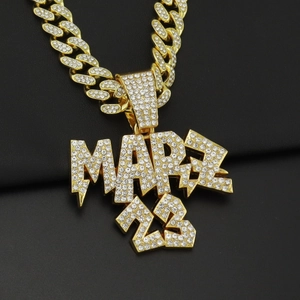 Gros plan du pendentif MARZ 23 hip-hop doré orné de cristaux blancs sur une chaîne cubaine