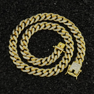 Gold-plated Cuban chain with iced-out pave rhinestones on a dark textured rock surface