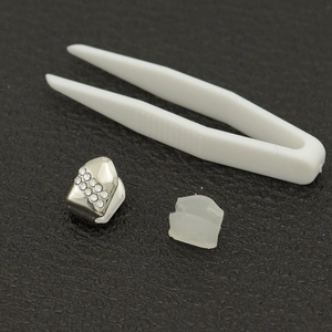 Détail de grillz dentaire plaqué or 18K avec strass, barre en silicone et pince blanche