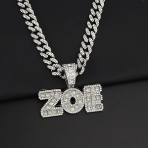 Primer plano del colgante con letra ZOE plateado y cristales sobre una cadena cubana
