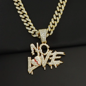 Macro detail of iced out NO LOVE pendant with broken heart on golden Cuban chain necklace