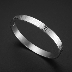 Macro detail of silver stainless steel bangle with engraved Roman numerals on black background