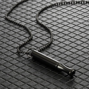 Macro shot of black stainless steel cylindrical whistle pendant necklace on textured surface