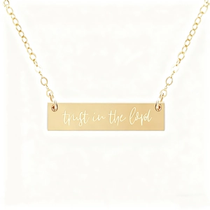 Detailed shot of gold bar necklace engraved with trust in the lord message