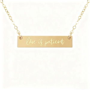 Macro shot of gold horizontal bar necklace engraved with Love is patient quote