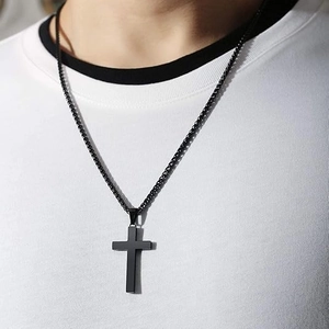 Detail of a matte black stainless steel cross pendant necklace on a white t-shirt