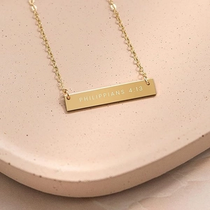 Detailed close-up of gold bar pendant with Philippians 4:13 engraving on a fine chain