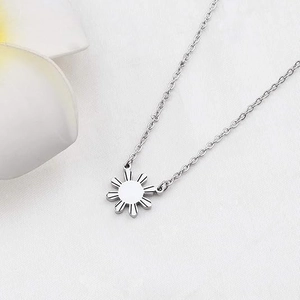 Détail du collier pendentif soleil avec lignes radiales sur fond de tissu blanc épuré