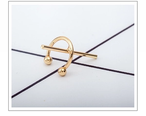 Macro detail of golden geometric C-shaped ear cuff with polished finish and ball ends