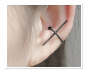 Macro view of a matte black C-shaped cross ear cuff on a female ear cartilage