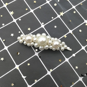 Detail of floral-shaped pearl hair clip with silver metal base on a mesh background