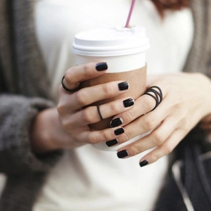 Three-piece set of minimalist matte black stackable rings worn on a hand holding a cup