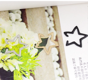 Three minimalist star-shaped ear clips in silver, gold, and black on a magazine page