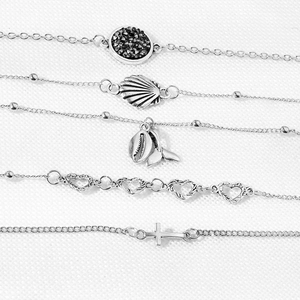 Detailed macro view of 5-piece silver charm bracelets with shells and cross pendants