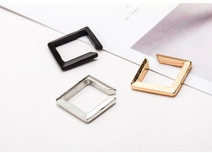 Macro view of minimalist square metal ear cuffs in black, silver, and gold finishes