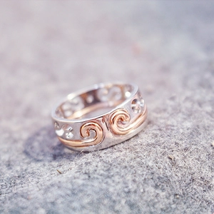 Macro view of silver and rose gold hollow pattern ring on a grey felt background