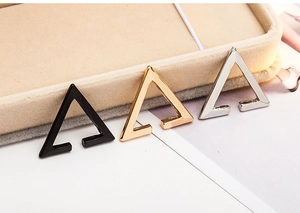 Close-up of geometric triangle ear clips in black, gold, and silver on a jewelry box