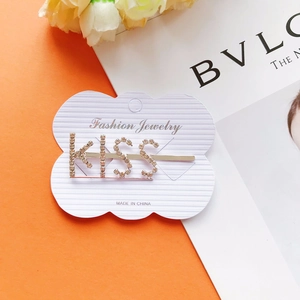 Dettaglio del fermaglio per capelli KISS dorato con strass su rivista di moda