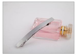 Detail of matte silver metal hair clip with brushed texture on a glass perfume bottle