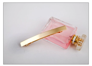 Close-up of golden bar hair clip with brushed texture on a transparent glass bottle