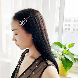 Dettaglio di un fermaglio dorato per capelli con scritta KISS e strass brillanti