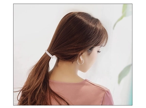 Detail of a pink matte metal hair clip styling a low ponytail with silver hoop earrings