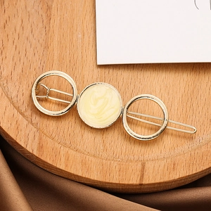 Détail d'une barrette dorée avec insert en marbre beige posée sur un plateau en bois