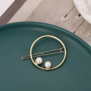 Detailed view of a gold round geometric hair clip with white pearls on a green tray