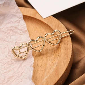 Eleganter goldener Haarclip mit drei hohlen Herzformen auf einem Holztablett