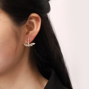 Detailed close-up of golden leaf-shaped earrings with pavé crystals on the ear lobe