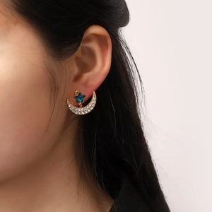 Elegant gold celestial moon and blue star crystal earrings shown on model's ear