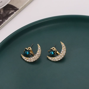 Star and moon studded earrings with blue crystal star and crystal moon on green plate