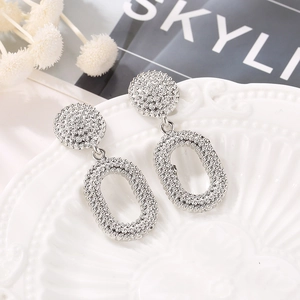 Vintage silver oval drop earrings with embossed texture on a ceramic display