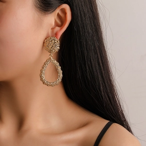 Close-up of model wearing chunky golden teardrop earrings with textured metallic finish