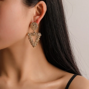 Macro detail of gold textured metal earrings with a geometric triangle drop design