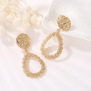 Golden alloy teardrop dangle earrings with irregular hammered texture on white tray