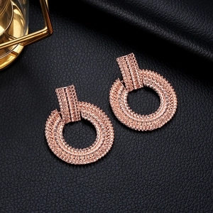 Dettaglio di orecchini a cerchio geometrici oro rosa con trame a diamante su pelle nera