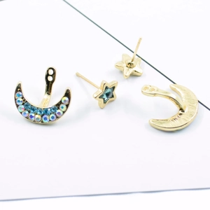 Detail of star and moon earrings with blue rhinestones and gold finish on white background