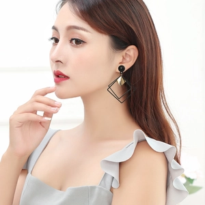 Close-up of geometric long dangle earrings with black square frames and gold accents